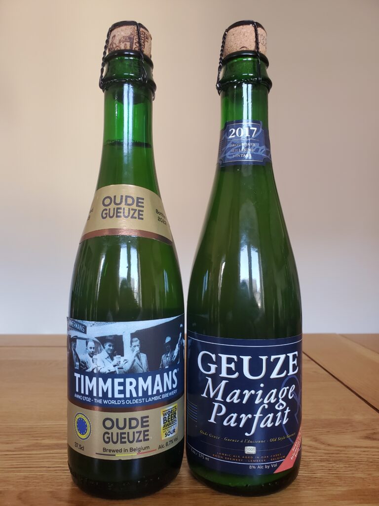 A bottle of Timmermans Oude Gueuze next to a bottle of Mariage Parfait beer.